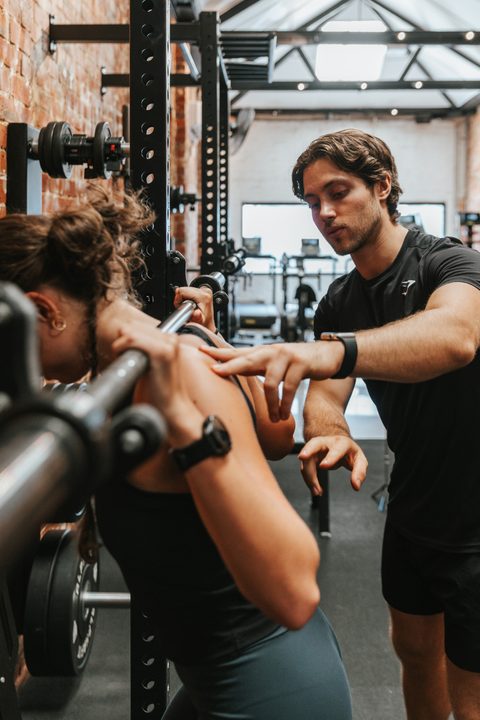 Jamie correcting a client's form on a barbell squats
